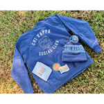 A blue crewneck that reads "Chi Kappa; Social Club" laying on grass with a white journal, two stickers and a blue knit beanie on top. All part of the Chi Kappa collection from Sierra Schultzzie.