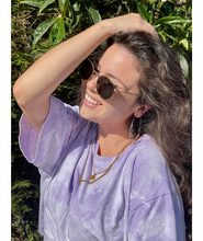Someone wearing the lavender confident and kind crop top from Sierra Schultzzie, facing the sunshine, wearing sunglasses an holding their arm up to their head, smiling. 