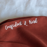 Confident & Kind” is in white curisve font along the lefthand pocket of copper colored pants - from Sierra Schultzzie