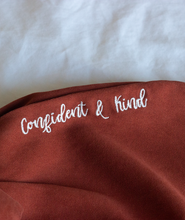 Confident & Kind” is in white curisve font along the lefthand pocket of copper colored pants - from Sierra Schultzzie