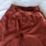 Copper colored pants with a copper colored belt tied in a knot. “Confident & Kind” is in white curisve font along the lefthand pocket - from Sierra Schultzzie