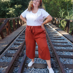 A woman modeling copper colored pants with a copper colored belt tied in a knot. “Confident & Kind” is in white curisve font along the lefthand pocket - from Sierra Schultzzie