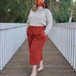 A woman modeling copper colored pants with a copper colored belt tied in a knot. “Confident & Kind” is in white curisve font along the lefthand pocket - from Sierra Schultzzie