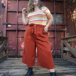 A woman modeling copper colored pants with a copper colored belt tied in a knot. “Confident & Kind” is in white curisve font along the lefthand pocket - from Sierra Schultzzie