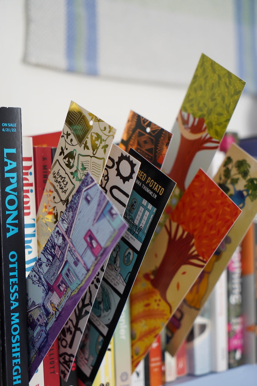 8 different illustrated, colorful bookmarks from the Books Unbound subscription poking out of books on a shelf. 
