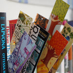 8 different illustrated, colorful bookmarks from the Books Unbound subscription poking out of books on a shelf. 