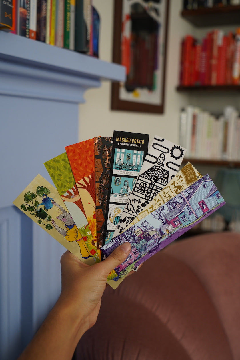 Someone holding a fan of 8 different illustrated, colorful bookmarks from the Books Unbound subscription. 