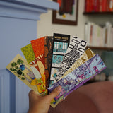 Someone holding a fan of 8 different illustrated, colorful bookmarks from the Books Unbound subscription. 