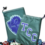 Two views (front and back) of a teal cloth dice bag with a drawstring closure. On one side of the bag is the blue text "TCC" in a block collegiate font. On the other side of the bag is an illustration of a crest -- a dragon's head peering at the pages of an open book. A pile of colorful dice (not included) sit below the bag.