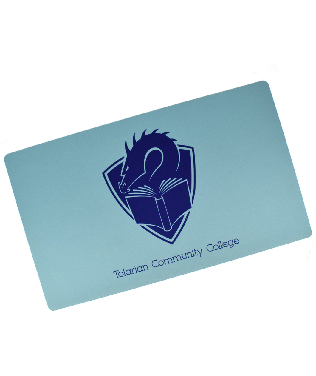 A rectangular mousepad-like mat in light blue. Centered on the mat is the TCC logo – a dragon's head peering at the pages of an open book, with a crest shape in the background. The blue text “Tolarian Community College” is below the logo.