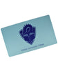 A rectangular mousepad-like mat in light blue. Centered on the mat is the TCC logo – a dragon's head peering at the pages of an open book, with a crest shape in the background. The blue text “Tolarian Community College” is below the logo.