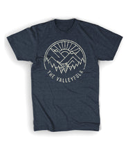 A navy shirt with a distressed circular logo of a white outline of mountains, a lake, trees, and a sun rising. “The Valleyfolk” is arched at the bottom in white sans serif font - from the Valleyfolk
