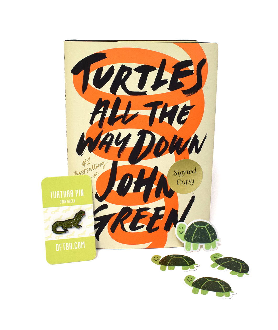 Book with orange spiral stretching height of cover on a cream background and black text that says “Turtles All the Way Down John Green.” A pin green tuatara pin leans against book. There are four green cartoon drawings of turtles with smiles - from John Green
