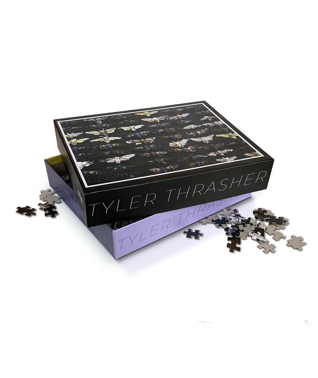 A black puzzle box lid with various cicadas on it sits atop a purple bottom puzzle box. Both boxes say "Tyler Thrasher" on them, and there are puzzle pieces scattered around the box.