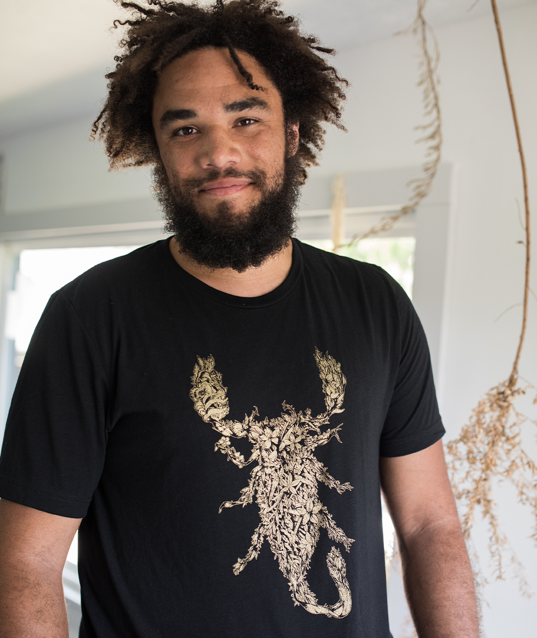 Tyler Thrasher modeling a dark gray shirt with white line drawn flowers arranged to make a scorpion in the center of the shirt - from Tyler Thrasher