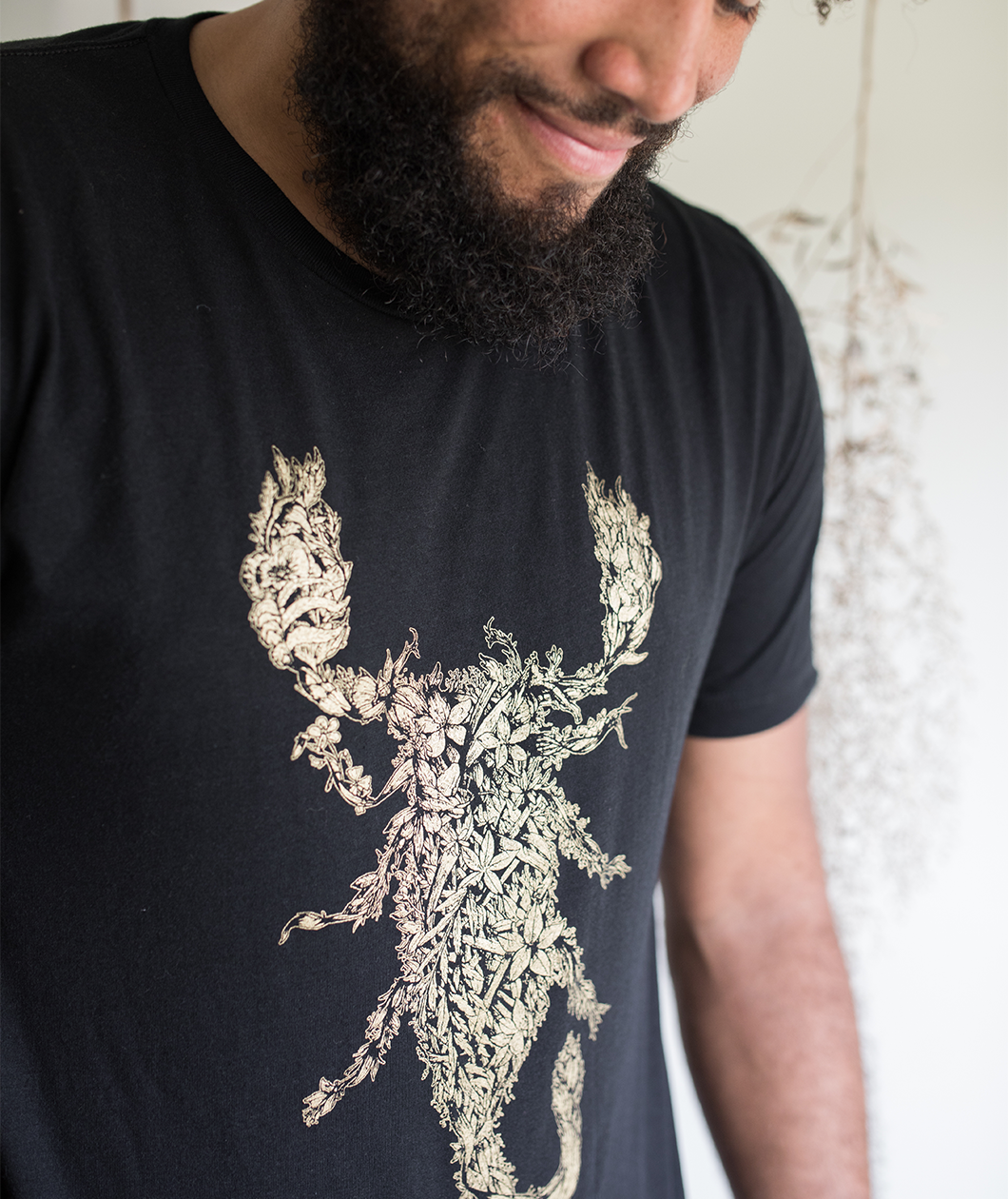 Tyler Thrasher modeling a dark gray shirt with white line drawn flowers arranged to make a scorpion in the center of the shirt - from Tyler Thrasher