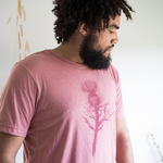 Tyler Thrasher modeling a red shirt with a dark red silhouette of a thistle weed in the center of the shirt. “Hands off” is written on the top of the thistle weed in red sans serif font - from Tyler Thrasher