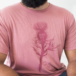Tyler Thrasher modeling a red shirt with a dark red silhouette of a thistle weed in the center of the shirt. “Hands off” is written on the top of the thistle weed in red sans serif font - from Tyler Thrasher
