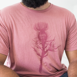 Tyler Thrasher modeling a red shirt with a dark red silhouette of a thistle weed in the center of the shirt. “Hands off” is written on the top of the thistle weed in red sans serif font - from Tyler Thrasher