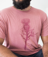 Tyler Thrasher modeling a red shirt with a dark red silhouette of a thistle weed in the center of the shirt. “Hands off” is written on the top of the thistle weed in red sans serif font - from Tyler Thrasher