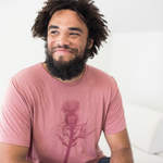 Tyler Thrasher modeling a red shirt with a dark red silhouette of a thistle weed in the center of the shirt. “Hands off” is written on the top of the thistle weed in red sans serif font - from Tyler Thrasher