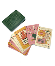 A set of Nerdfighter playing cards. There is a face down stack with a dark green pattern on the card. There is a also a fan of cards laid out in a warm pastel color scheme with different illustrations on them. 